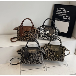 Detail view of four plush leopard print Boston handbags in various colors on a white stand