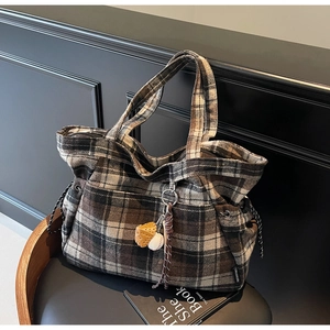 Detail of wool-textured plaid tote bag with baseball charm on a vintage chair