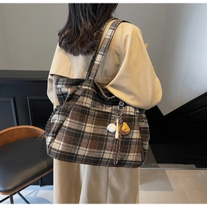 Retro brown plaid tote bag with baseball charm shown on shoulder with khaki trench coat