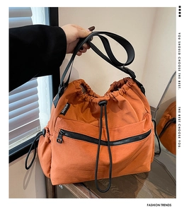 Detail of orange nylon bucket bag showing drawstring closure and black zipper pocket