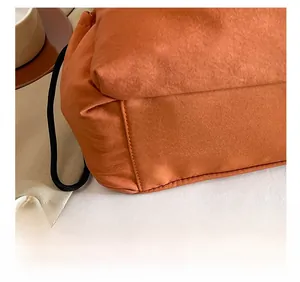 Detail view of precise stitching and wrinkled nylon texture on the orange bucket bag