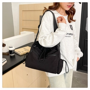 Detail of black nylon bucket bag with drawstring closure and wide woven shoulder strap