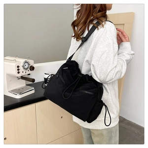 Detail of black nylon drawstring bucket bag with side zipper and fashion label on the strap