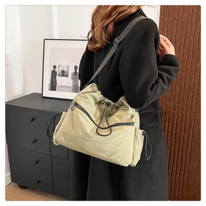 Detail of khaki nylon drawstring bucket bag with black zipper pockets and adjustable strap