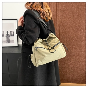 Detail of khaki nylon bucket bag with drawstring closure and black shoulder strap on model