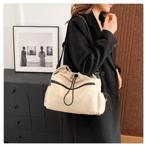Detail of beige nylon drawstring bucket bag with black zippers and shoulder strap