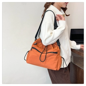 Detail of vibrant orange nylon bucket bag with black drawstrings and adjustable strap