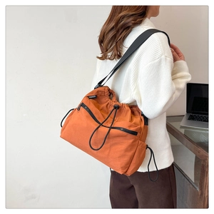 Detail view of orange nylon bucket bag featuring drawstring closure and fashion label