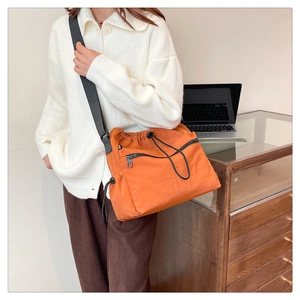 Detail shot of orange nylon bucket bag featuring drawstring closure and black zipper pocket