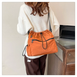 Detail of a bright orange nylon drawstring bucket bag with black zipper and fashion label