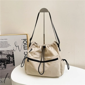 Minimalist nylon drawstring bucket bag in beige with black zipper pocket and shoulder strap