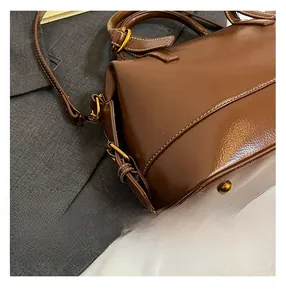 Détail du sac en cuir marron montrant les coutures blanches et les pieds métalliques