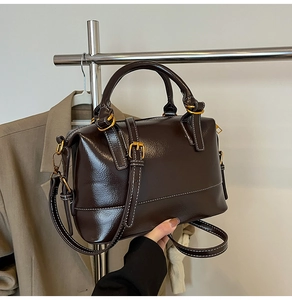 Détail du sac Boston en cuir marron foncé avec coutures blanches et finitions dorées
