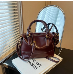 Détail du sac Boston bordeaux avec surpiqûres blanches et garnitures dorées