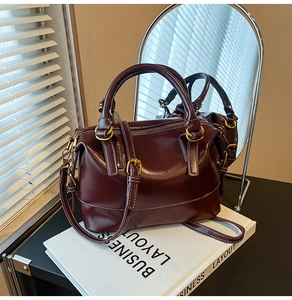 Détail du sac boston en cuir brillant bordeaux avec coutures blanches et finitions dorées