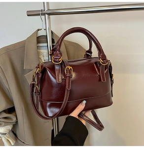 Détails d'un sac à main bordeaux brillant avec boucles dorées et coutures blanches