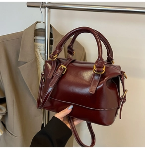 Détail d'un sac Boston en cuir verni rouge foncé avec ferrures dorées et surpiqûres