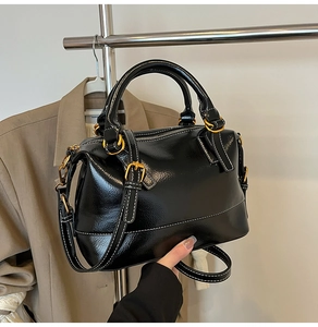Détail d'un sac à main en cuir verni noir avec boucles dorées et coutures blanches