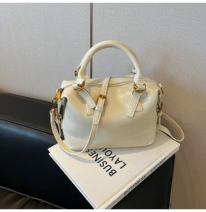 Détail du sac Boston crème avec ferrures dorées et bandoulière posé sur un livre