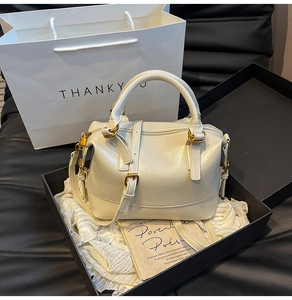Détail d'un sac Boston crème avec texture cuir et boucles dorées dans son coffret cadeau