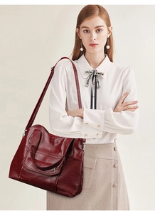 Deep burgundy large tote bag with multiple zippers and adjustable shoulder strap on model