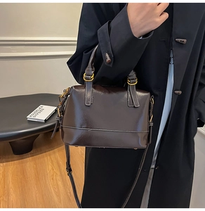 Détail d'un sac Boston en cuir ciré marron foncé avec surpiqûres blanches et métal doré