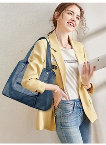 Detail view of deep blue leather tote bag with zip pocket worn by a fashion model