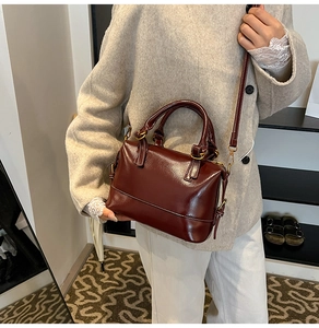 Détail du sac Boston marron rouge brillant avec ferrures dorées et bandoulière réglable