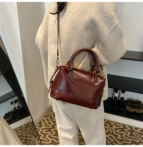 Détail de la texture en cuir ciré bordeaux et finitions dorées du sac Boston