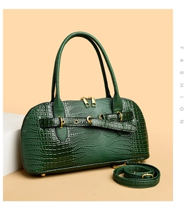 Detail view of dark green crocodile texture handbag with gold buckles and dual zippers