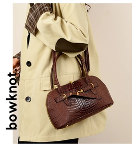 Detail of dark brown crocodile embossed leather bag with golden horsebit buckle
