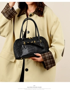 Detail of black embossed leather handbag with crocodile pattern and gold zipper hardware