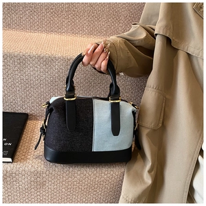 Detailed close-up of contrast denim boston bag with leather handles and gold hardware
