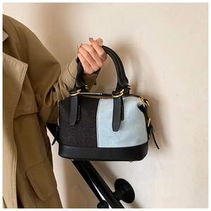 Boston bag with denim patchwork and black leather handles shown by model on stairs