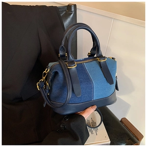 Detail of blue denim Boston bag featuring navy leather contrast and gold hardware