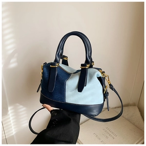 Detail of color-block denim Boston bag with dark blue leather trim and golden hardware