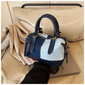 Detail of color-block denim Boston bag with navy leather handles and gold hardware