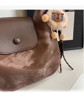Detail der braunen Vintage-Schultertasche mit weicher Textur und Plüsch-Anhänger