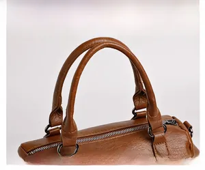 Détail d'un sac à main marron à grain litchi montrant les poignées et anneaux en métal