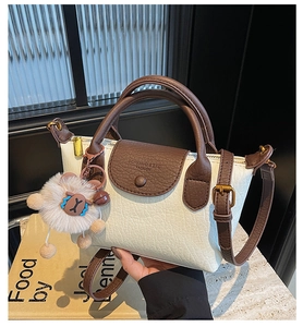Close-up of the cream dumpling bag with brown leather accents and a plush lamb charm