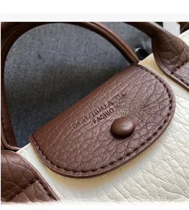 Detail of lychee textured leather with embossed logo on contrast color dumpling bag