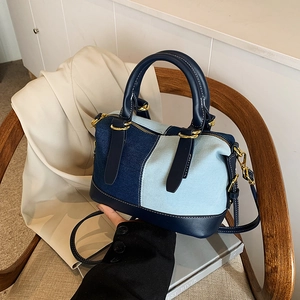 Chic patchwork denim Boston bag with leather handles shown on a rustic wooden chair