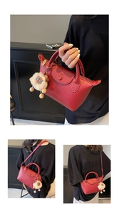 Detail of red lychee leather handbag featuring gold logo and cute lion plush charm accessory