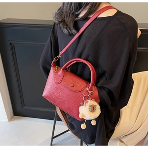 Detail of red textured leather handbag with detachable strap and plush charm