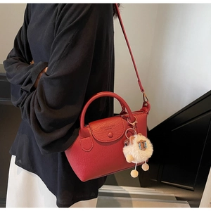 Detail der roten Handtasche aus genarbtem Leder mit Klappenverschluss und Löwenanhänger