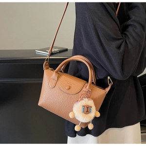 Detailansicht der braunen Lederhandtasche mit Logo-Prägung und Plüsch-Lamm-Anhänger