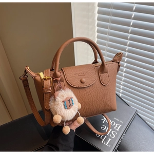Detailansicht der braunen Handtasche aus Leder mit Plüschschaf-Anhänger und Gurt