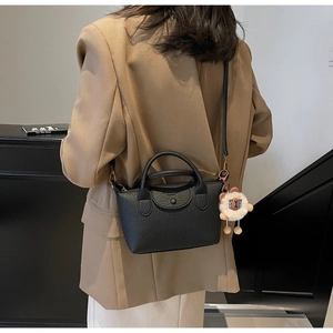 Black pebbled leather bag on model featuring adjustable strap and white sheep plush charm