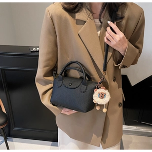 Detail of black leather handbag with dual handles and cute plush sheep charm