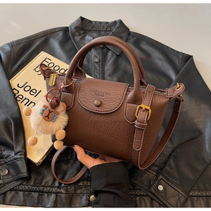 Detail einer dunkelbraunen Lederhandtasche mit Bronze-Hardware und Glockenanhänger